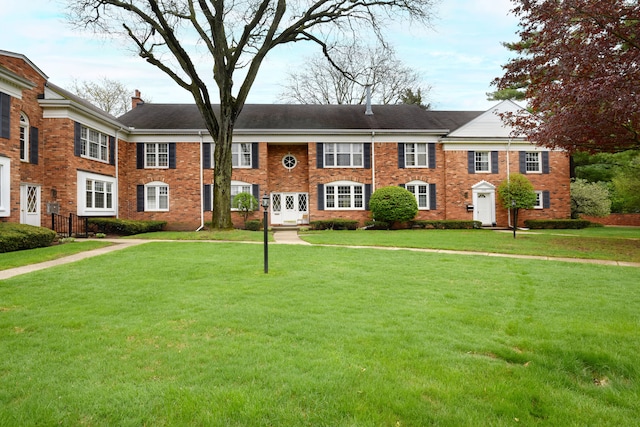 view of front of house featuring a chimney, a front yard, and brick siding