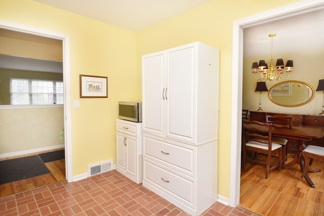 corridor with baseboards, a chandelier, and brick patterned flooring