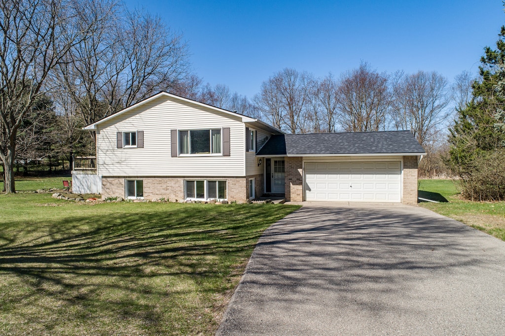 tri-level home featuring brick siding, a front lawn, aphalt driveway, and a garage
