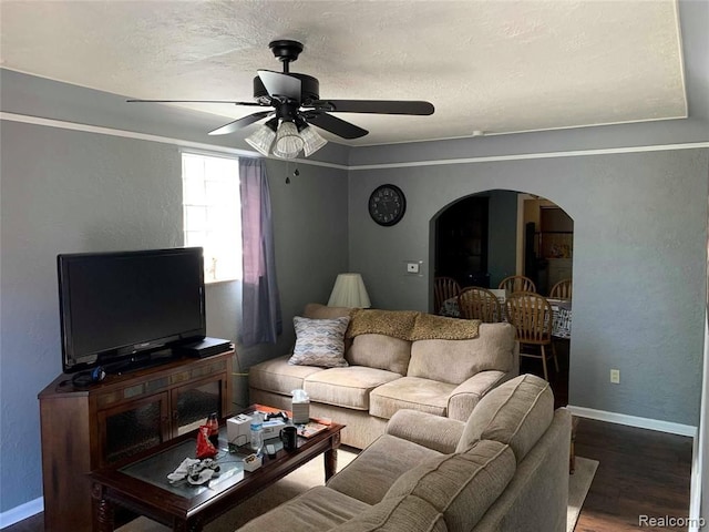 living area featuring arched walkways, baseboards, wood finished floors, ceiling fan, and a textured wall