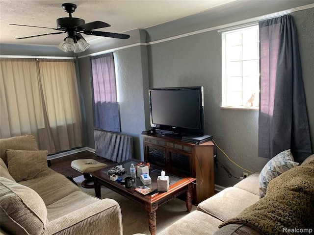 living area featuring radiator heating unit, a textured wall, a ceiling fan, and wood finished floors