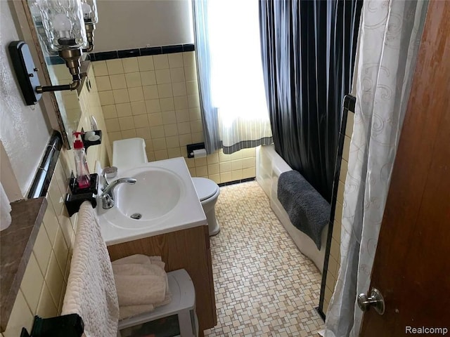bathroom with toilet, vanity, a wainscoted wall, and tile walls