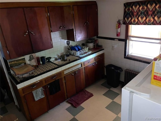 kitchen featuring a sink, tile walls, radiator heating unit, light floors, and tile countertops