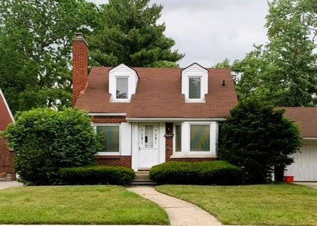 cape cod-style house featuring a chimney, brick siding, and a front yard