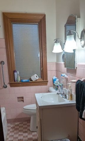 bathroom featuring a wainscoted wall, tile patterned floors, toilet, vanity, and tile walls