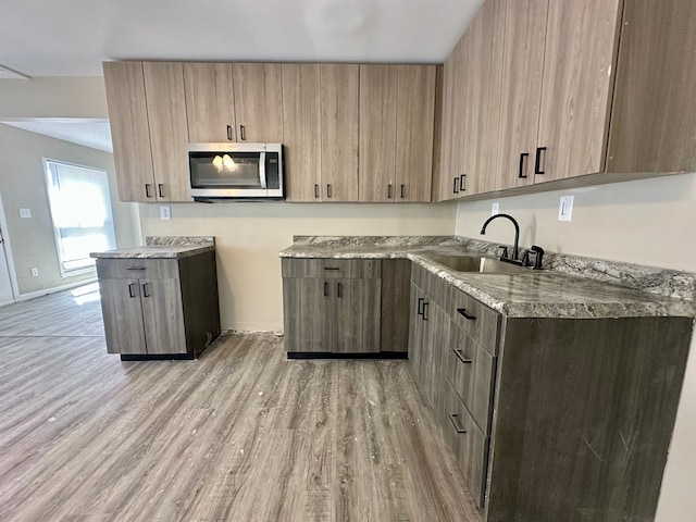 kitchen featuring light stone countertops, stainless steel microwave, light wood finished floors, a sink, and baseboards