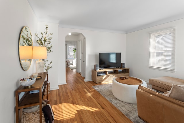 living area featuring arched walkways, baseboards, and light wood-type flooring