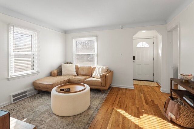living area featuring visible vents, arched walkways, light wood-style floors, and a healthy amount of sunlight