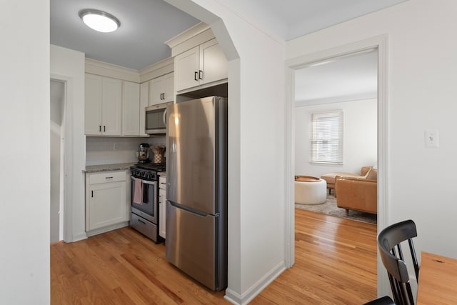 kitchen with decorative backsplash, white cabinetry, arched walkways, light wood-style flooring, and appliances with stainless steel finishes