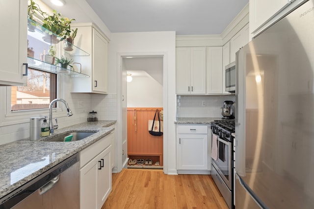 kitchen featuring open shelves, a sink, light wood-style flooring, stainless steel appliances, and white cabinetry