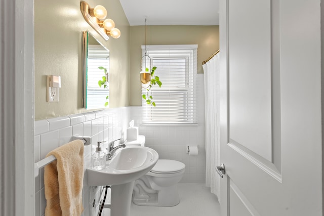 bathroom with a wainscoted wall, tile patterned floors, toilet, and tile walls