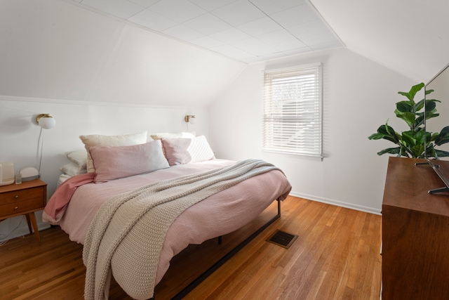 bedroom featuring visible vents, baseboards, lofted ceiling, and wood finished floors