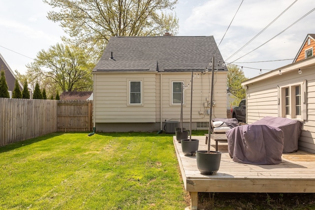 rear view of house with a shingled roof, a deck, a fenced backyard, central AC unit, and a yard