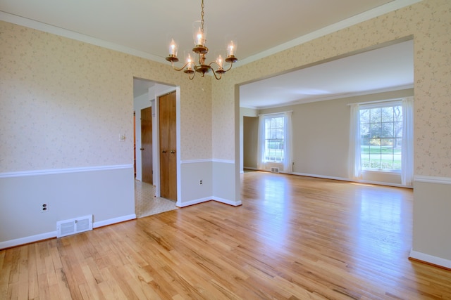 spare room featuring light wood-style floors, a notable chandelier, crown molding, visible vents, and wallpapered walls
