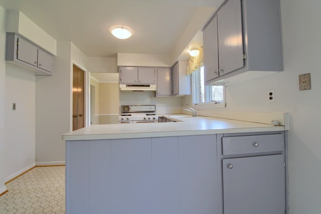 kitchen featuring under cabinet range hood, white range with gas stovetop, gray cabinets, a peninsula, and light countertops