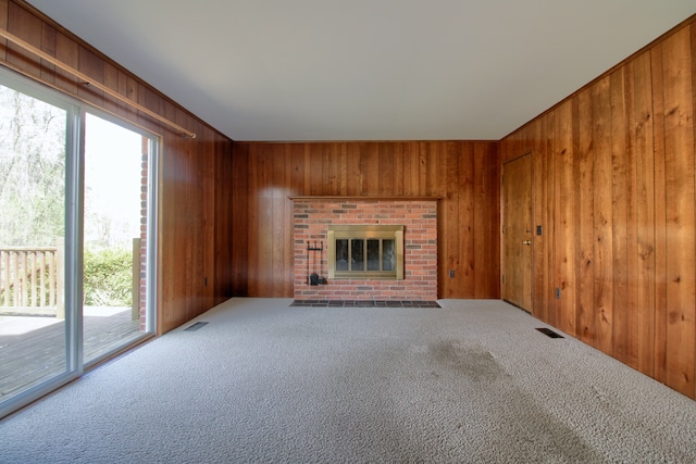unfurnished living room with wood walls, a wealth of natural light, visible vents, and carpet