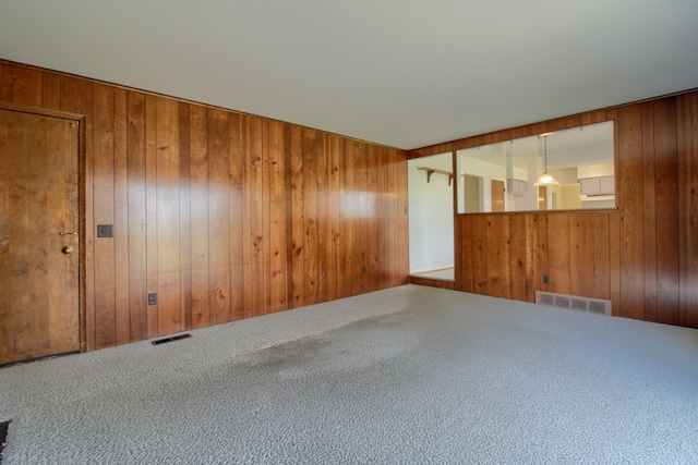 spare room featuring wooden walls, visible vents, and carpet flooring