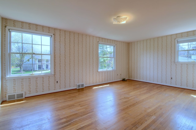 spare room with visible vents, hardwood / wood-style floors, wallpapered walls, and a healthy amount of sunlight