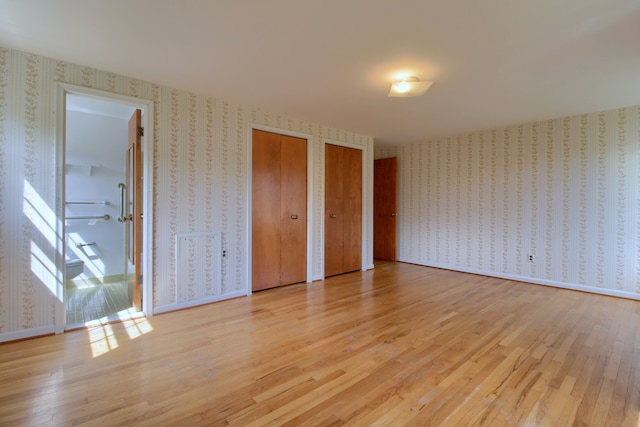 unfurnished bedroom with multiple closets, light wood finished floors, and wallpapered walls