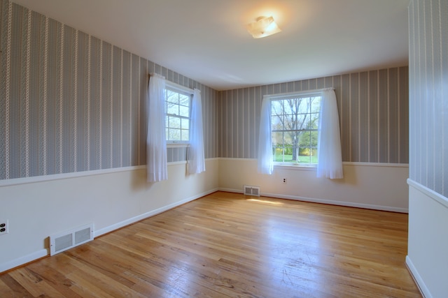 empty room featuring wood finished floors, visible vents, and wallpapered walls