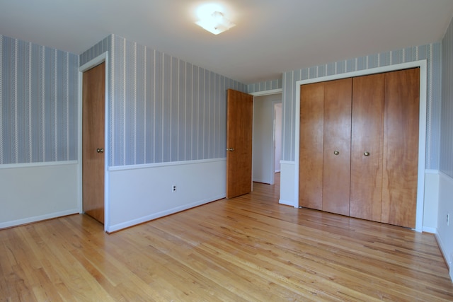 unfurnished bedroom featuring baseboards, wallpapered walls, wood finished floors, and a closet
