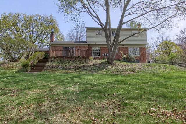 back of house with a chimney, a deck, brick siding, stairs, and a lawn
