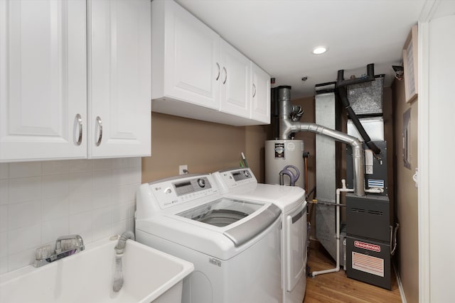 washroom featuring a sink, water heater, cabinet space, light wood-style flooring, and washing machine and dryer