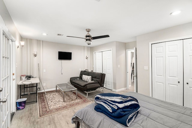 bedroom featuring two closets, baseboards, visible vents, and wood finished floors