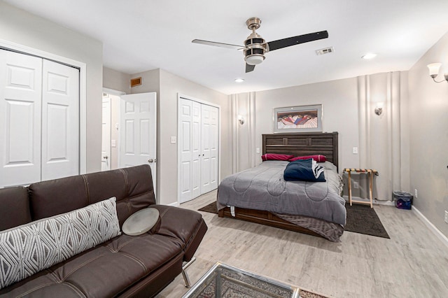bedroom with ceiling fan, visible vents, wood finished floors, baseboards, and two closets