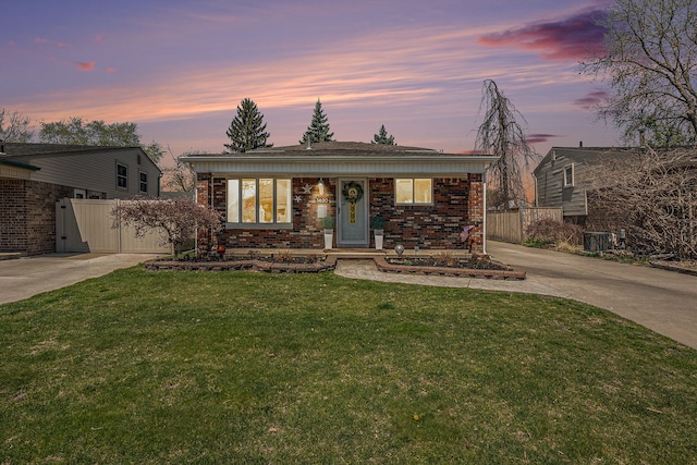 view of front of home featuring fence, brick siding, a front yard, and concrete driveway