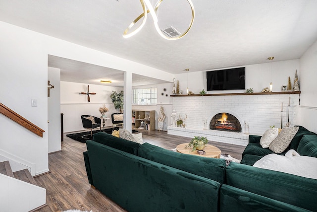 living room featuring visible vents, wood finished floors, a brick fireplace, and stairs