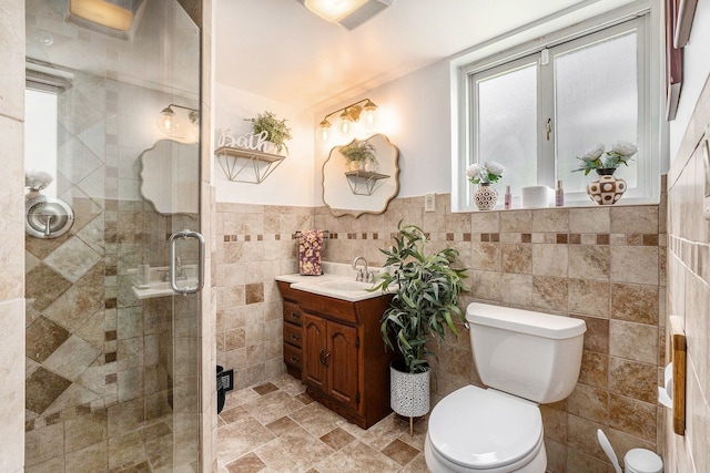 full bathroom featuring stone finish floor, toilet, vanity, tile walls, and a stall shower