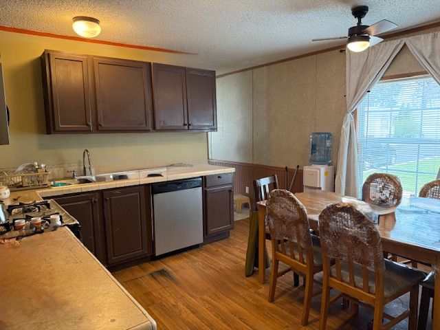 kitchen with stainless steel dishwasher, a sink, a textured ceiling, light wood-type flooring, and light countertops