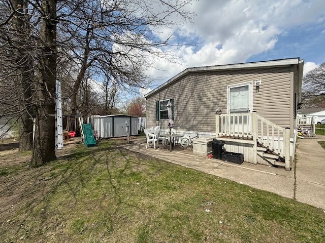 rear view of property featuring a patio area, a lawn, an outdoor structure, and a shed