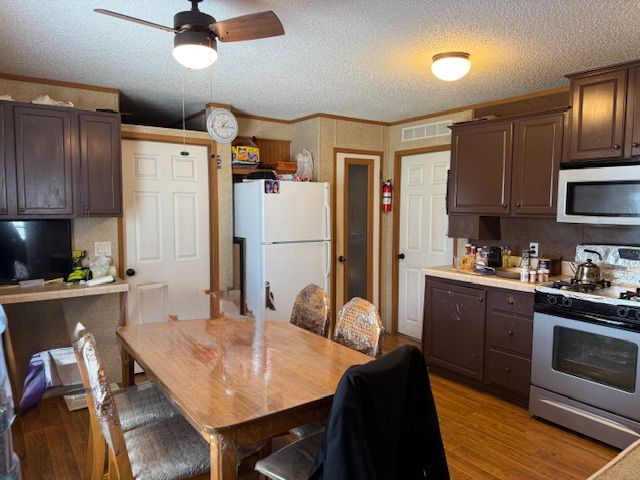 kitchen with a textured ceiling, dark brown cabinetry, gas range oven, stainless steel microwave, and freestanding refrigerator