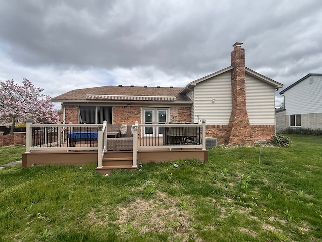 back of house featuring a chimney, a yard, brick siding, a shingled roof, and a wooden deck