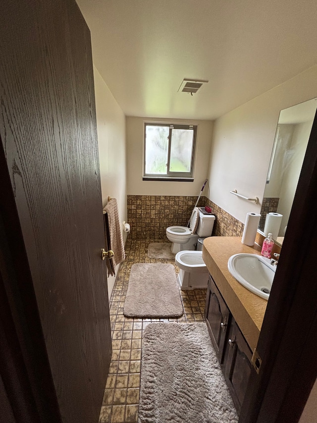 bathroom featuring vanity, toilet, visible vents, wainscoting, and a bidet