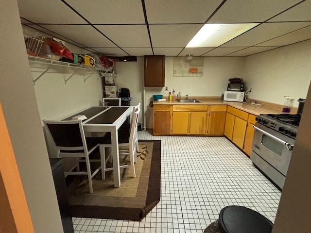 kitchen featuring high end stove, a sink, white microwave, light countertops, and a drop ceiling