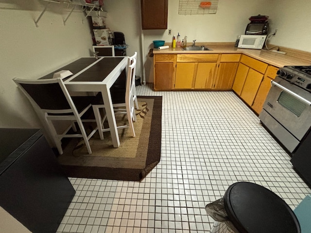 kitchen featuring white microwave, light tile patterned floors, light countertops, a sink, and stainless steel gas range