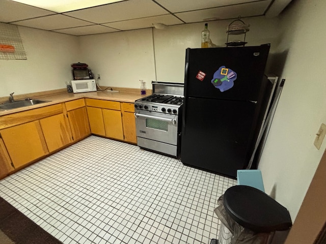 kitchen featuring a sink, stainless steel range with gas stovetop, white microwave, light countertops, and freestanding refrigerator