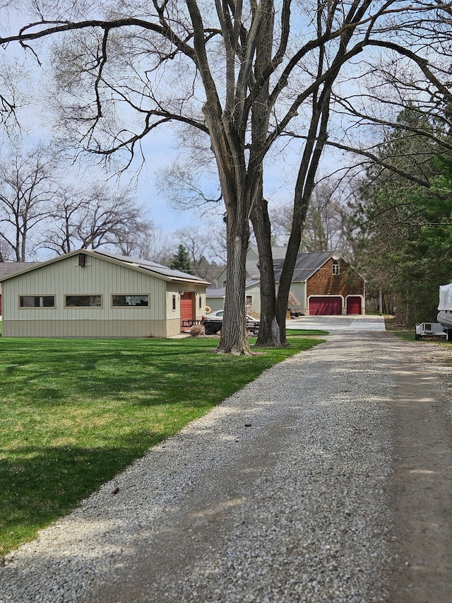 exterior space featuring gravel driveway, board and batten siding, a detached garage, and a front yard