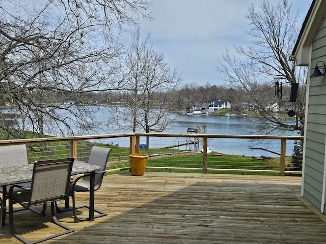 wooden terrace with outdoor dining area, a water view, and a lawn
