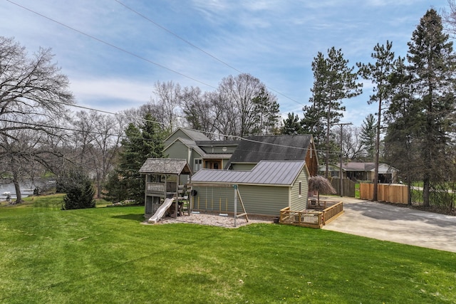 back of property featuring a playground, a lawn, concrete driveway, fence, and metal roof