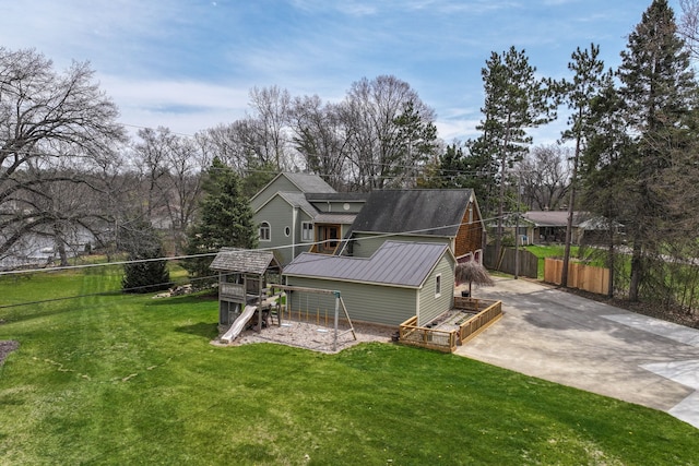 rear view of property with a playground, a lawn, concrete driveway, fence, and a wooden deck