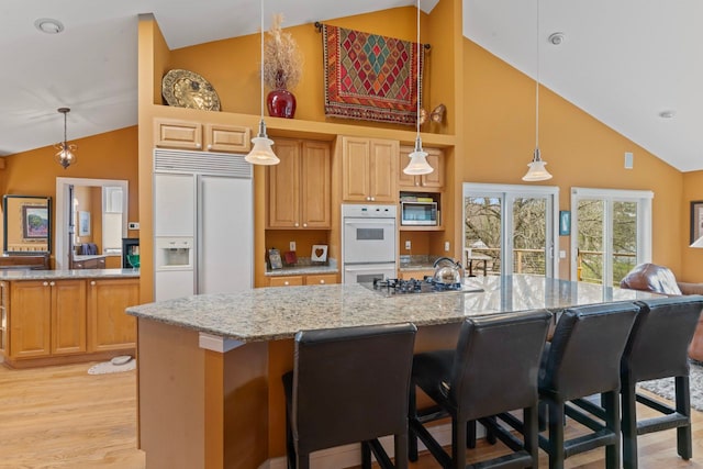 kitchen featuring light wood finished floors, an island with sink, light stone counters, built in appliances, and high vaulted ceiling