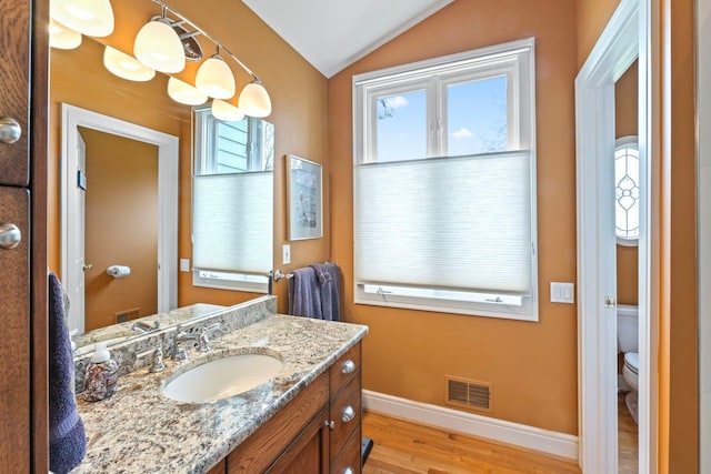 bathroom with wood finished floors, baseboards, toilet, lofted ceiling, and visible vents