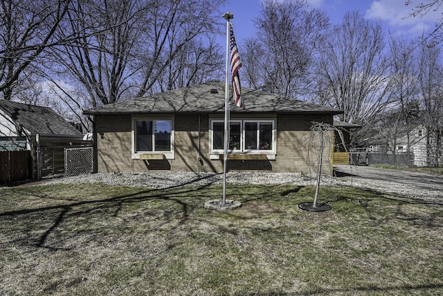 rear view of property with a lawn, fence, roof with shingles, and brick siding