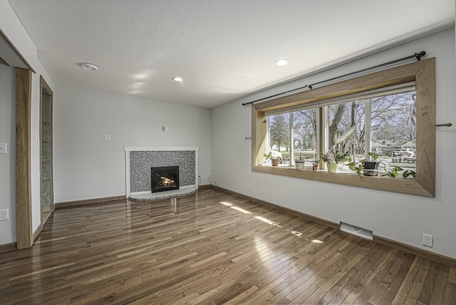 unfurnished living room featuring a glass covered fireplace, visible vents, recessed lighting, baseboards, and hardwood / wood-style flooring