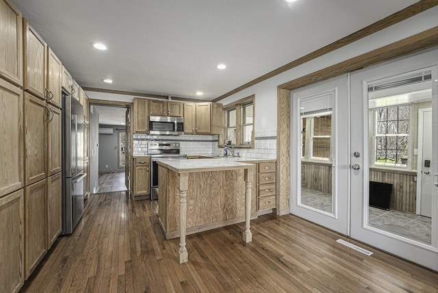 kitchen with light countertops, crown molding, a peninsula, appliances with stainless steel finishes, and dark wood-style flooring