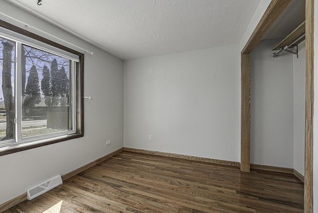 interior space featuring a textured ceiling, baseboards, visible vents, and dark wood-style floors